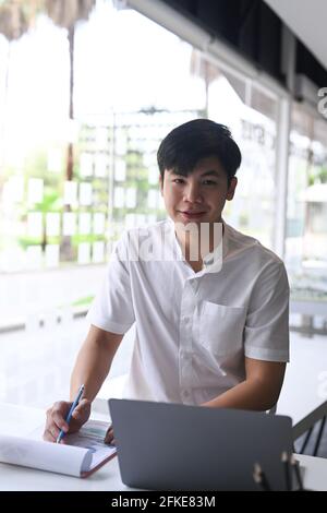 Porträt eines lächelnden Geschäftsmannes, der im modernen Büro sitzt und vor der Kamera lächelt. Stockfoto