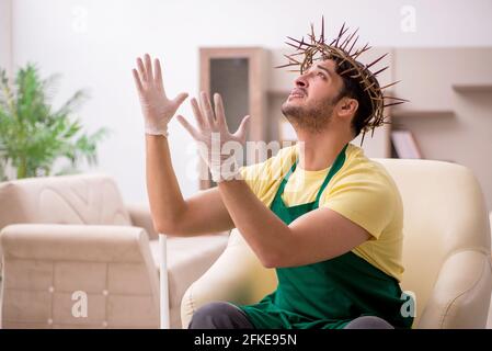 Junger männlicher Auftragnehmer, der auf dem Kopf einen stacheligen Kranz trägt und Hausarbeit leistet Stockfoto
