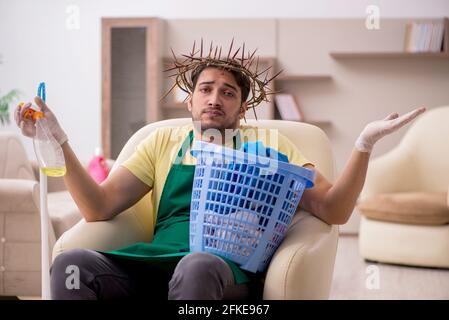 Junger männlicher Auftragnehmer, der auf dem Kopf einen stacheligen Kranz trägt und Hausarbeit leistet Stockfoto