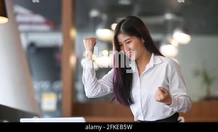 Eine aufgeregte Geschäftsfrau, die im Büro vor ihrem Computer-Laptop steht und das Erfolgsergebnis feiert. Stockfoto