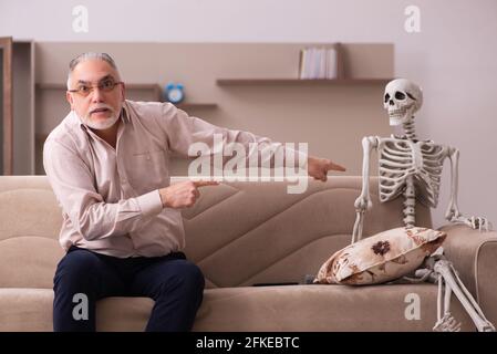 Alter Mann sitzt auf dem Sofa mit dem weiblichen Skelett In unsterbst Liebe Konzept Stockfoto