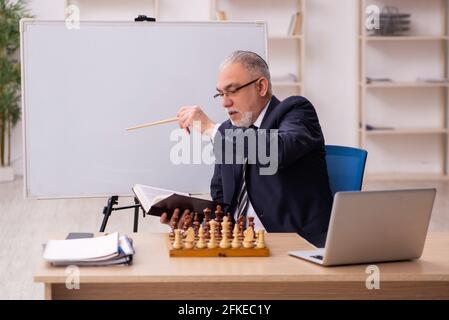 Alter Geschäftsmann Angestellter, der Schach am Arbeitsplatz spielt Stockfoto