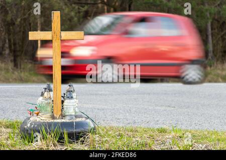 Ein Gedenkkreuz am Straßenrand mit Kerzen zum Gedenken an den tragischen Tod, auf einer Fahrt im Hintergrund verschwommenes Auto. Stockfoto