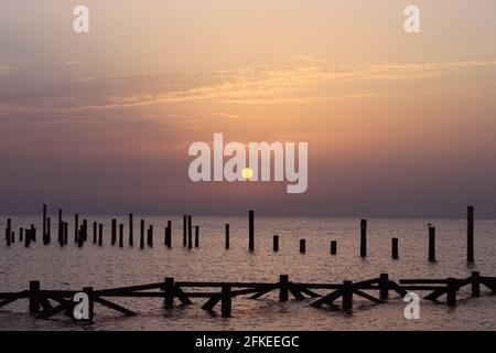 Sonnenaufgang auf dem Meer. Holzstapel von zerstörten Pier ragen aus dem Wasser. Morgensonne. Rotes Meer, Safaga, Ägypten. Stockfoto