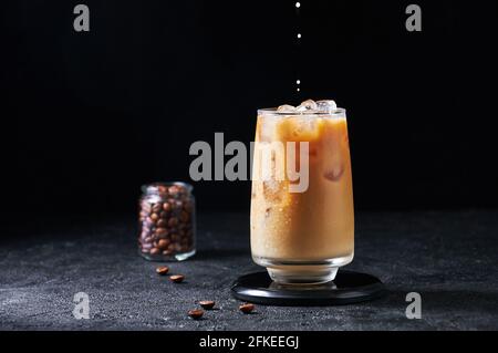 Milch, Die in Eiskaffee in Hochgläserem Glas auf dunklem Hintergrund Gegossen wird. Konzept Erfrischendes Sommergetränk. Stockfoto