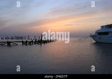 Sonnenaufgang auf dem Meer. Der Himmel ist in Rosa-Tönen gehalten. Hölzerne Stapel von alten zerstörten Pier, die aus Wasser und Schiff ragen. Früh am Morgen Sonne appe Stockfoto