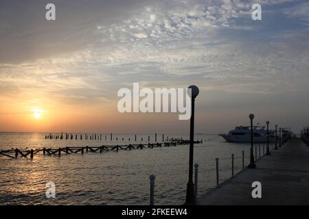 Sonnenaufgang auf dem Meer. Pier, der sich bis in die Unendlichkeit erstreckt und das Boot in der Ferne. Holzstapel von alten zerstörten Pier ragen aus dem Wasser. Boote auf Stockfoto