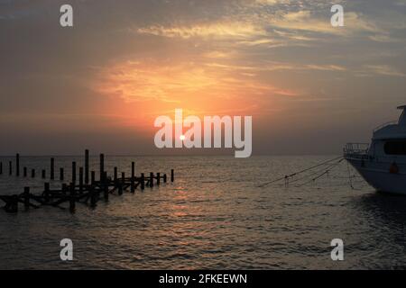 Schöner Sonnenuntergang am Meer. Hölzerne Stapel zerstörter Pier ragen aus dem Wasser und dem Boot. Warme Sonnenstrahlen. Stockfoto