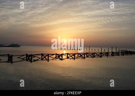 Schöner Sonnenuntergang am Meer. Hölzerne Stapel von alten zerstörten Pier ragen aus dem Wasser und dem Schiff in der Ferne. Warme Sonnenstrahlen. Stockfoto