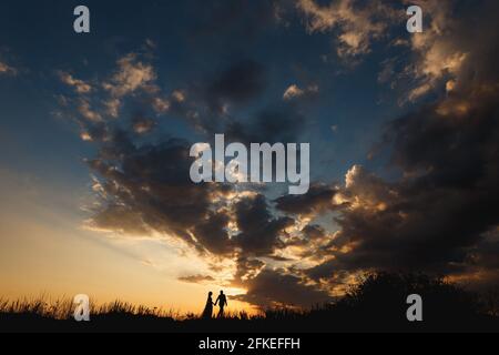 Mann und Frau gehen mit den Händen vor dem Hintergrund Von einem wunderschönen Sonnenuntergang Himmel Stockfoto
