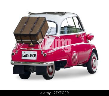 Ein kleines Retro-Auto mit einem Koffer auf der Rückseite ist bereit für eine Reise, isoliert auf einem weißen Hintergrund. Stockfoto