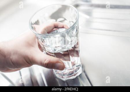 Hand ein mit Wasser gefülltes Trinkglas anhalten Ein Küchenwaschbecken Stockfoto