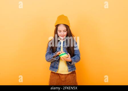 Ein Mädchen in einem mehrfarbigen Hemd hält ein mehrfarbiges, slinky Spielzeug In ihren Händen Stockfoto