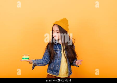 Ein Mädchen in einem mehrfarbigen Hemd hält ein mehrfarbiges, slinky Spielzeug In ihren Händen Stockfoto