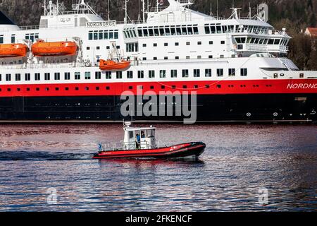 Kleines Arbeitsboot Polarcirkel, das im Hafen von Bergen, Norwegen, ankommt. Im Hintergrund ist die Küstenfähre Trollfjord (Hurtigruten) zu sehen. Stockfoto