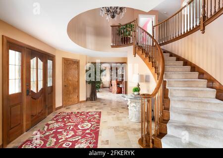 Ein schöner Eingang mit einer Wendeltreppe, einer kreisförmigen Öffnung im zweiten Stock und einem Kronleuchter. Der Blick geht zum Esszimmer. Stockfoto