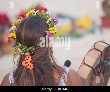 Rückansicht einer jungen Frau mit Kranzblumen auf dem Kopf, die bei einem gesellschaftlichen Ereignis an einem tropischen Strand in Mexiko die Trommel spielt Stockfoto