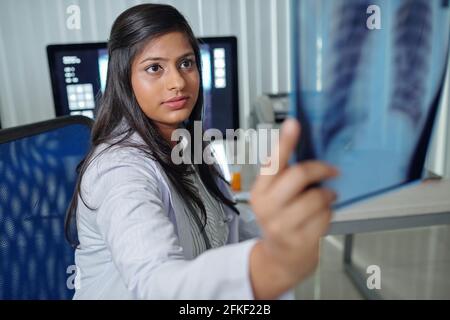 Ein ziemlich junger indischer Radiologe, der die Röntgenaufnahme des Patienten untersucht Behandelt für Coronavirus Stockfoto