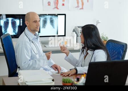 Pneumologen diskutieren schwierigen Fall, sie sitzen im Raum mit Röntgenaufnahmen der Brust auf Computerbildschirmen Stockfoto