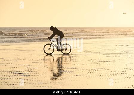 Ein Mann, der mit dem Fahrrad auf dem Sand in der Tiefsand fährt Gezeiten am Strand von Hove