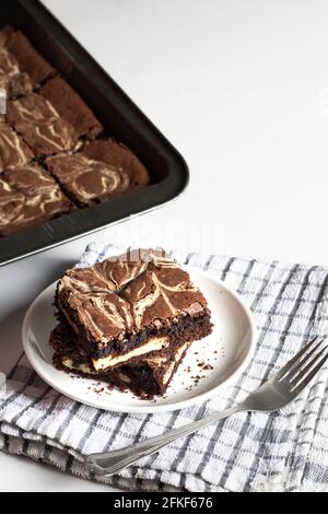 Zwei Käsekuchen-Brownies auf einem weißen Teller mit einem Brownies Fach im Hintergrund Stockfoto