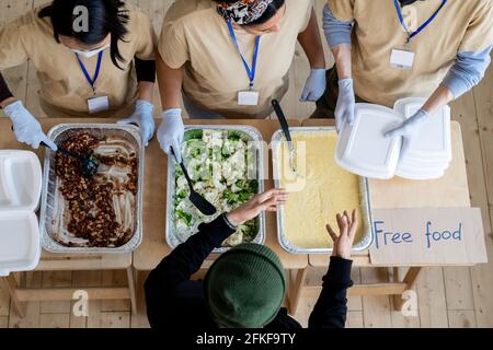 Junge Freiwillige geben den Menschen Behälter mit kostenlosem Essen In Not Stockfoto