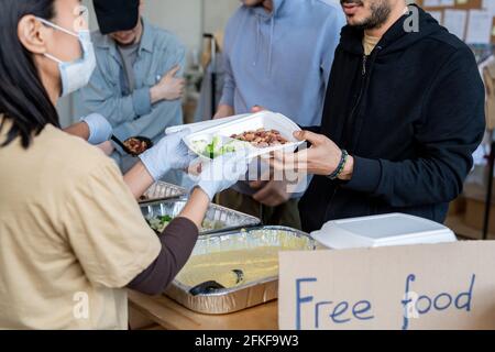 Freiwillige in Handschuhen und Masken, die Flüchtlingen kostenloses Essen servieren Oder Obdachlose Stockfoto