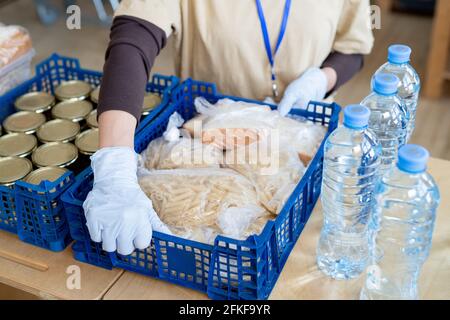 Ein Freiwilliger, der mit einem Gestachel aufliegt und eine große Schachtel mit Lebensmitteln auf den Tisch legt Stockfoto