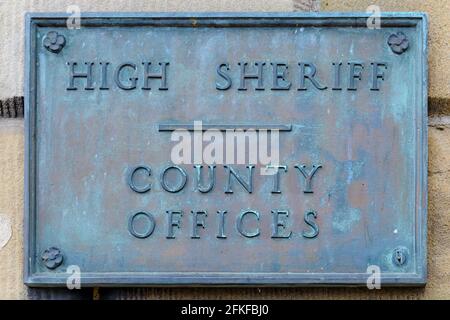 Ein antikes verwittertes Kupfer- oder Messingschild mit erhabenen Buchstaben, die hohe SHERIFF COUNTY-BÜROS sagen. Das Schild ist auf einem Gebäude und mit dem Alter angeschmutzt. Stockfoto