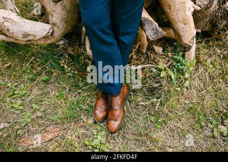 Beine eines Mannes in einem blauen Anzug und braune Lederschuhe stehen auf trockenem Gras, Nahaufnahme Stockfoto