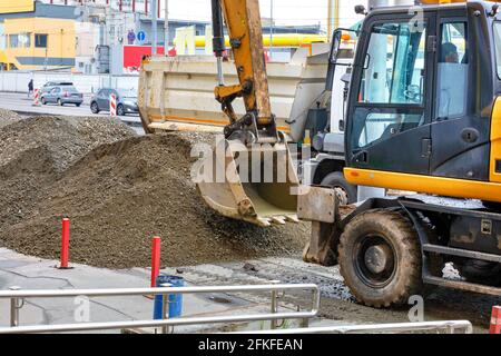 Straßenbagger arbeitet auf dem Bürgersteig und lädt Sand auf den LKW. Stockfoto