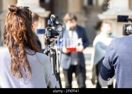 Weibliche Kamerafrau, die mit einer Videokamera ein Medienereignis oder eine Nachrichtenkonferenz dreht. Public Relations - PR-Konzept. Stockfoto