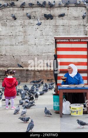 Ältere Frau verkauft Vogelfutter mit jungen Mädchen, die Tauben füttern In Istanbul Stockfoto