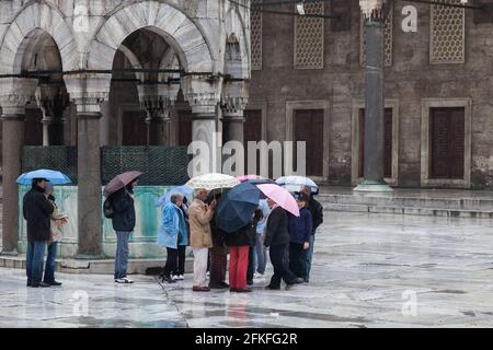 Touristen stehen im Regen unter Sonnenschirmen an der Blauen Moschee in Istanbul Stockfoto