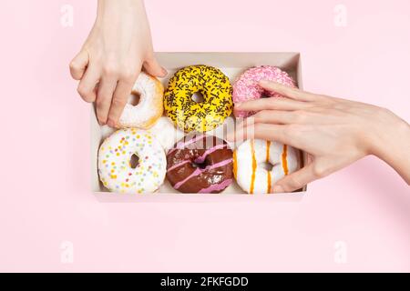 Hände nehmen farbige glasierte Donuts in Donut-Box. Hände greifen verschiedene Geschmacksrichtungen Donuts. Ungesunde Snacks im Büro oder in einer Pausenstation. Stockfoto