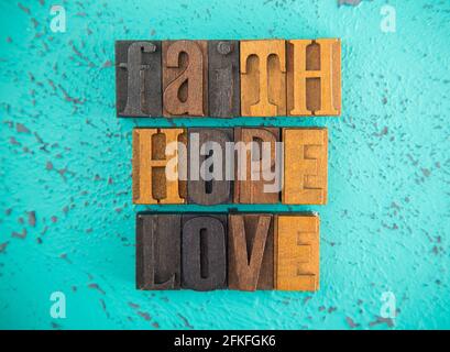 Faith Hope and Love geschrieben in Holzart Set Block Buchstaben auf türkisfarbenem Hintergrund Stockfoto