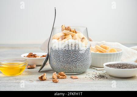 Das Bananendessert wird aus Chiasamen mit Kokosmilch, Nüssen und Honig auf hellem Hintergrund hergestellt. Gesunder, natürlicher Vitaminpudding. Seitenansicht. Stockfoto