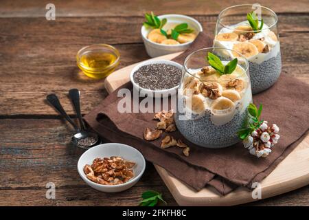 Gesunder Pudding mit Kokosmilch, Chiasamen, Banane, Nüssen und Honig auf braunem Hintergrund. Seitenansicht mit Kopierbereich. Stockfoto