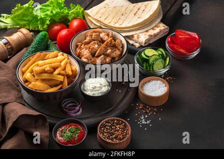 Gebratenes Huhn, Pommes Frites, Gemüse, Sauce, Pita-Brot und Gewürze auf braunem Hintergrund. Zutaten für Shawarma, Burrito, Gyros. Fast Food. Stockfoto