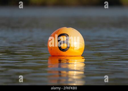 Leuchtend orange Boje schwimmt im See mit Wasserspiegelung. Das Schild mit der Nummer 8 ist acht auf der Seite aufgedruckt, auf der der Behälter für Boote markiert ist. Stockfoto