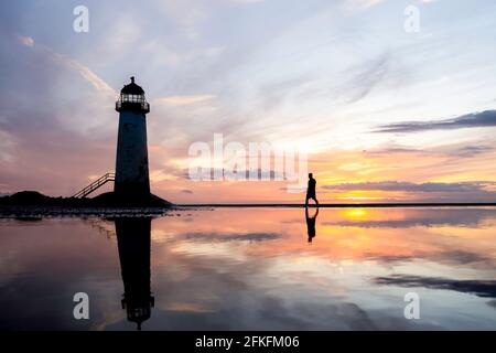 Leuchtturm steht im Wasserbecken atemberaubende Sonnenuntergangsreflexion im Meerwasser reflektiert. Einzelmann, der die Küste von Nordwales erkundet, Sand am Strand Stockfoto