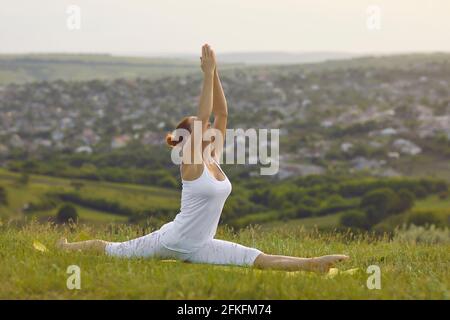 Reife Frau, die Hanumanasana macht, während sie Yoga auf frischem Grün praktiziert Wiese auf dem Land Stockfoto