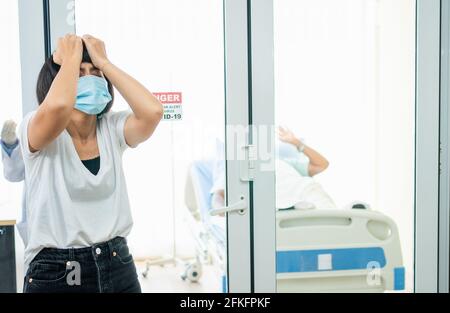 Eine Frau, die vor dem Quarantäneraum steht und Ihren Kopf mit ihren Händen hält, während sie auf die Untersuchungsergebnisse wartet, hat Angst. Konzept Stockfoto