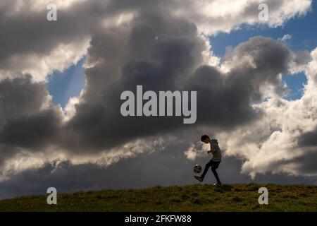 Langshaw Scottish Borders, Großbritannien. Mai 2021. UK UK Weather EIN kleiner Junge praktiziert seine Anhalten-Uppies auf Gras in Langshaw an der schottischen Grenze, mit dramatischen dunklen Regenwolken als Hintergrund. Die Wettervorhersage für die Feiertage sieht nicht vielversprechend aus, da ein Großteil des Vereinigten Königreichs die ersten signifikanten Niederschläge seit langem erwartet, willkommen für Gärtner und Landwirte, aber nicht für diejenigen, die das lange Wochenende der Feiertage am 1. Mai genießen möchten. Quelle: phil wilkinson/Alamy Live News Stockfoto