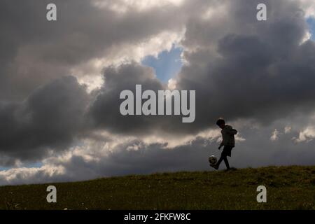 Langshaw Scottish Borders, Großbritannien. Mai 2021. UK UK Weather EIN kleiner Junge praktiziert seine Anhalten-Uppies auf Gras in Langshaw an der schottischen Grenze, mit dramatischen dunklen Regenwolken als Hintergrund. Die Wettervorhersage für die Feiertage sieht nicht vielversprechend aus, da ein Großteil des Vereinigten Königreichs die ersten signifikanten Niederschläge seit langem erwartet, willkommen für Gärtner und Landwirte, aber nicht für diejenigen, die das lange Wochenende der Feiertage am 1. Mai genießen möchten. Quelle: phil wilkinson/Alamy Live News Stockfoto