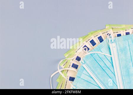 Medizinische Gesichtsmaske und Bargeld. Einweg-OP-Schutzmasken und Euro-Banknoten auf grauem Hintergrund. Draufsicht Stockfoto