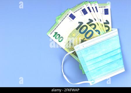 Rund hundert Euro-Banknoten, eingewickelt in eine Einweg-OP-Gesichtsmaske auf hellgrauem Hintergrund. Draufsicht Stockfoto