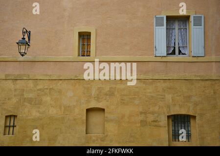 Hausfassade im Provençal-Stil mit ockerfarbener Stuckwand und einem Fenster mit Spitzenvorhängen und hölzernen Fensterläden in Aix-en-Provence Marseille, Frankreich. Stockfoto