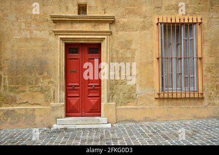 Hausfassade im Provençal-Stil mit ockerfarbener Stuckwand, einer leuchtend roten Tür und einem Fenster mit hölzernen Fensterläden in Aix-en-Provence Marseille, Frankreich. Stockfoto