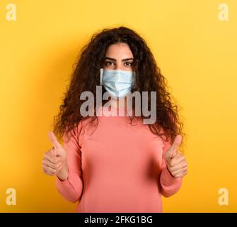 Mädchen ist optimistisch über die Niederlage von covid 19 Coronavirus. Gelber Hintergrund. Stockfoto